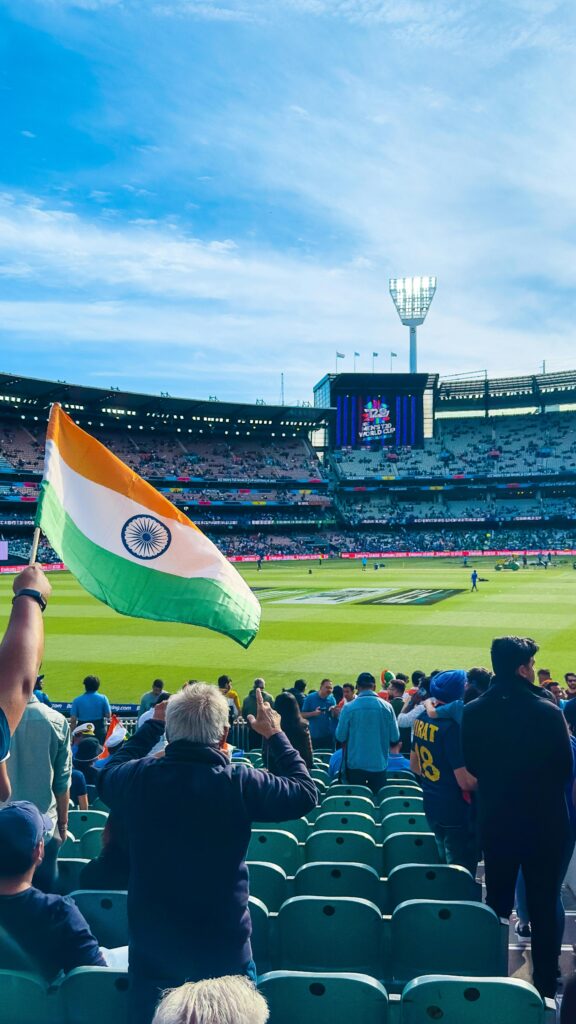 Excited fans waving the Indian flag at Melbourne Cricket Ground during a cricket match.