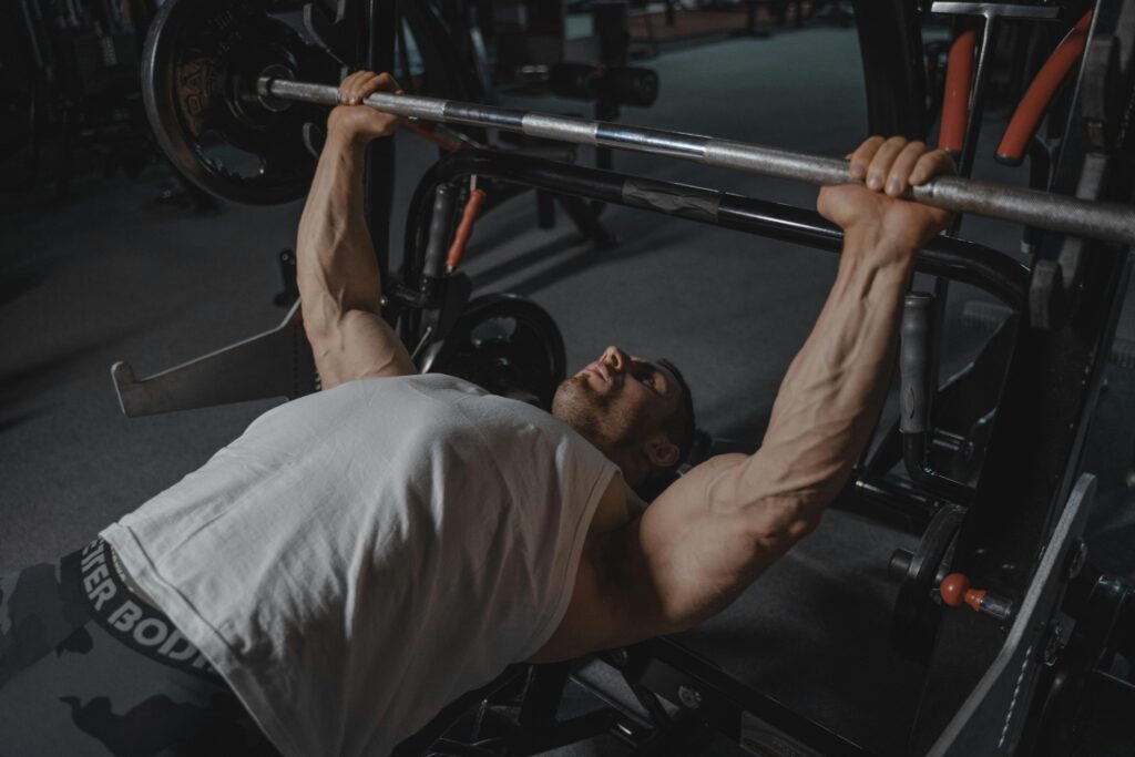 pexels-photo-5327556-5327556 A focused man lifts heavy weights on a bench press machine in a dimly lit gym.